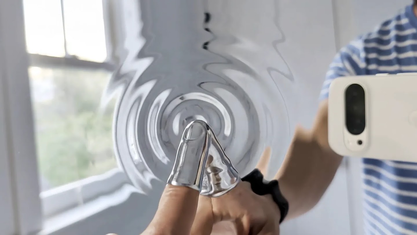 A finger touching a mirror, the reflection turning to liquid chrome with ripples spreading out